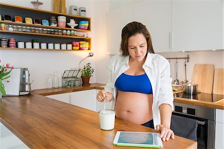 female belly button pictures - Pregnant woman eats yogurt while using tablet Stock Photo - Premium Royalty-Free, Code: 6115-08149228