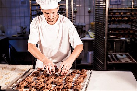 Confectioner positioning chocolate cookies on baking tray Foto de stock - Sin royalties Premium, Código: 6115-08100493