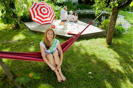Woman sitting on hammock, family in background, Munich, Bavaria, Germany Stock Photo - Premium Royalty-Free, Code: 6115-08100621