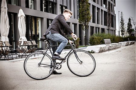 Young businessman riding bicycle on city street, Munich, Bavaria, Germany Stock Photo - Premium Royalty-Free, Code: 6115-08100751