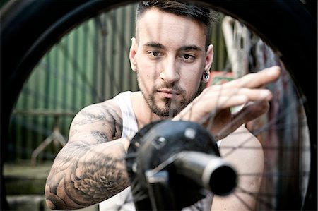 photos of tattooed people on bicycles - Young man in workshop repairing bicycle tire Stock Photo - Premium Royalty-Free, Code: 6115-08101031