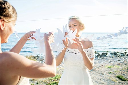 simsearch:6115-08239477,k - Bride and bridesmaid playing with white paper cut out outdoors Stock Photo - Premium Royalty-Free, Code: 6115-08239476