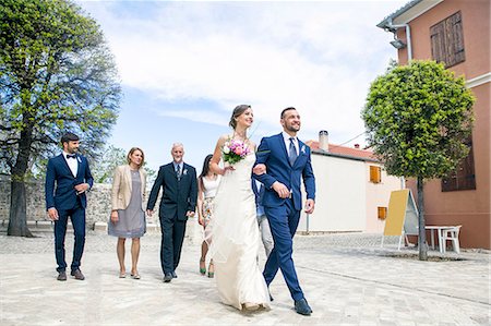 simsearch:6115-08239477,k - Bride and groom walking with family in background Stock Photo - Premium Royalty-Free, Code: 6115-08239405