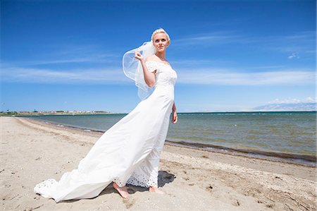 simsearch:6115-08239440,k - Bride in wedding dress standing on beach Foto de stock - Royalty Free Premium, Número: 6115-08239430