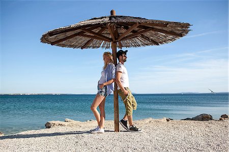 simsearch:6115-08239576,k - Young couple standing under parasol on beach Stock Photo - Premium Royalty-Free, Code: 6115-08239576