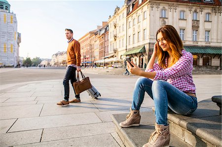 Mid adult woman using smart phone with man in background Stock Photo - Premium Royalty-Free, Code: 6115-08416247