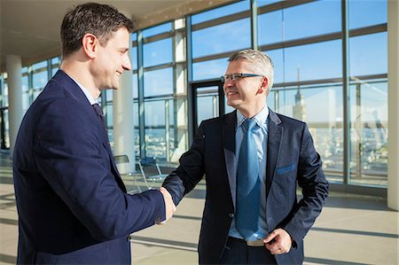 simsearch:6115-08416334,k - Two businessmen shaking hands in modern office Fotografie stock - Premium Royalty-Free, Codice: 6115-08416320