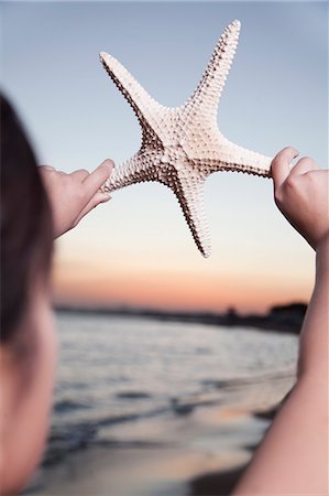 Teenage girl looking and holding up starfish Photographie de stock - Premium Libres de Droits, Code: 6116-06939037