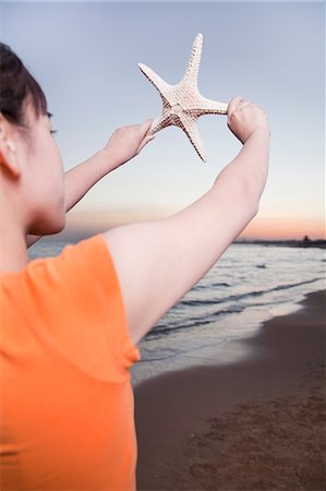 Teenage girl looking and holding up starfish Stock Photo - Premium Royalty-Free, Code: 6116-06939036