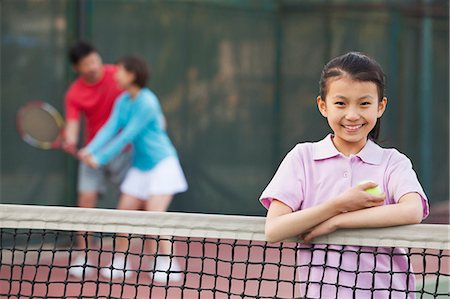 daughter standing next to the tennis net, parents playing in the background Stock Photo - Premium Royalty-Free, Code: 6116-06939318