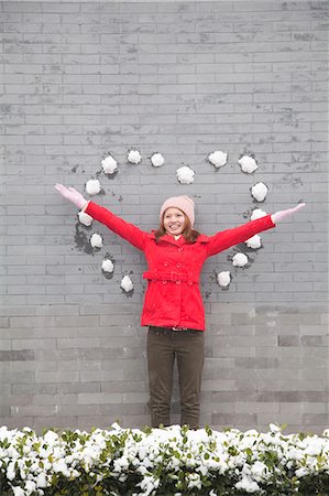 smiling women inviting - Young woman standing on wall with heart shaped snow balls Stock Photo - Premium Royalty-Free, Code: 6116-06939542