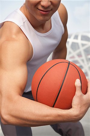 Young man showing bicep and holding basketball Stock Photo - Premium Royalty-Free, Code: 6116-07084596