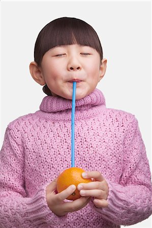 Portrait of young girl drinking an orange with a straw, studio shot Stock Photo - Premium Royalty-Free, Code: 6116-07084714
