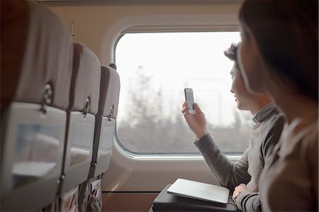 simsearch:6116-07085094,k - Young man sitting on a train taking a photo out the window Foto de stock - Sin royalties Premium, Código: 6116-07085900