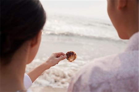 simsearch:6116-07085909,k - Young couple standing and looking at seashell on the beach, over the shoulder view Stock Photo - Premium Royalty-Free, Code: 6116-07085907