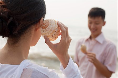 Young couple looking at seashells, holding shell to ear Stock Photo - Premium Royalty-Free, Code: 6116-07085908