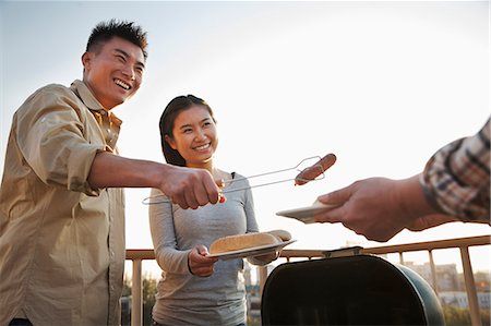 family barbeque outdoors - Son giving sausage to his father over the barbeque Photographie de stock - Premium Libres de Droits, Code: 6116-07086114