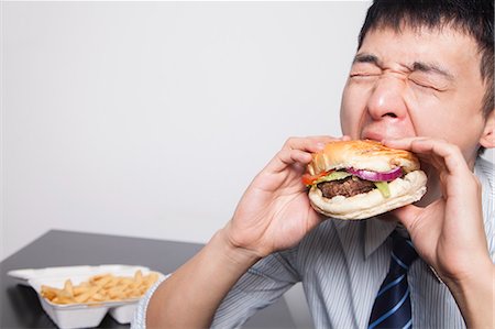 eating fries - Young businessman enjoying a burger Stock Photo - Premium Royalty-Free, Code: 6116-07086730