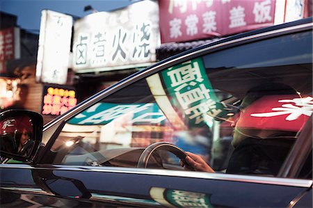 Young man driving through Beijing at night, illuminated store signs reflected off the windows of the car Foto de stock - Sin royalties Premium, Código: 6116-07235793