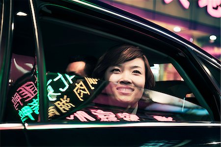 reflection of woman in car - Smiling businesswoman with car window rolled down looking out at the nightlife in Beijing Stock Photo - Premium Royalty-Free, Code: 6116-07235794