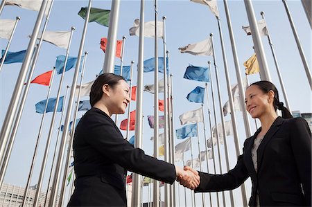 poteau porte-drapeau - Two businesswomen shaking hands with flags in background. Photographie de stock - Premium Libres de Droits, Code: 6116-07235822