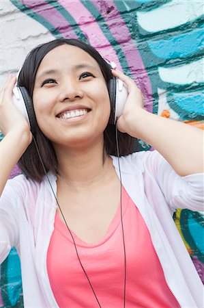 simsearch:614-07587649,k - Young smiling woman holding her headphones while enjoying listening to music in front of wall with graffiti Stockbilder - Premium RF Lizenzfrei, Bildnummer: 6116-07235958
