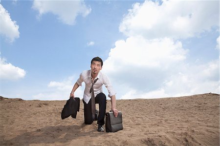 Young businessman kneeling in the desert and holding a briefcase, exhausted Foto de stock - Sin royalties Premium, Código: 6116-07235974