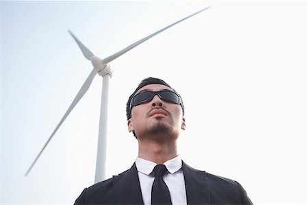 suit man asian - Portrait of serious young businessman in sunglasses standing by a wind turbine Foto de stock - Sin royalties Premium, Código: 6116-07235980