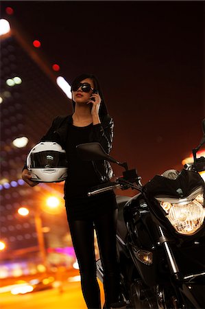 Young woman in sunglasses talking on the phone and standing beside her motorcycle at night in Beijing Stock Photo - Premium Royalty-Free, Code: 6116-07235904