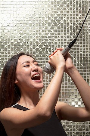 Young woman singing into a microphone at karaoke, shiny background Foto de stock - Sin royalties Premium, Código: 6116-07236060