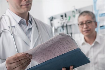 simsearch:6116-07236099,k - Doctor checking medical chart with patient in the background Photographie de stock - Premium Libres de Droits, Code: 6116-07236074