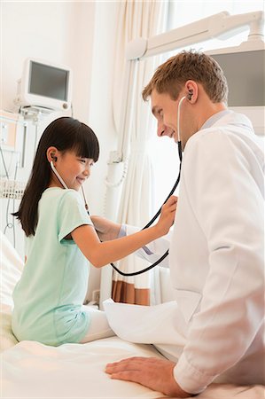 Girl patient checking the doctors heart beat with a stethoscope on a hospital bed Foto de stock - Sin royalties Premium, Código: 6116-07236095