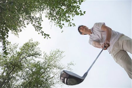 simsearch:6116-07236128,k - Low angle view of man getting ready to hit the golf ball on the golf course Foto de stock - Sin royalties Premium, Código: 6116-07236037