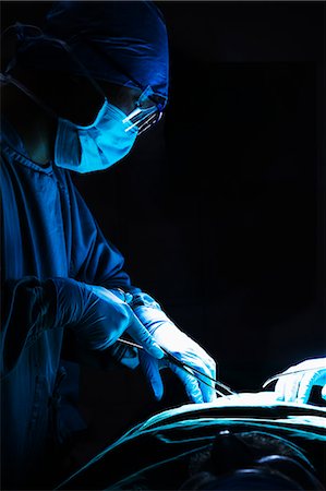 Surgeon looking down, working, and holding surgical equipment with patient lying on the operating table Photographie de stock - Premium Libres de Droits, Code: 6116-07236157
