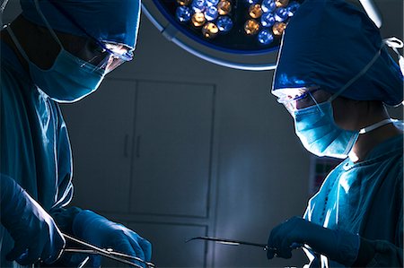 eyeglasses focus - Two surgeons looking down and working at the operating table, dark operating room Stock Photo - Premium Royalty-Free, Code: 6116-07236155