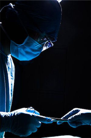 Two surgeons working and passing surgical equipment in the operating room, dark, close-up Photographie de stock - Premium Libres de Droits, Code: 6116-07236160