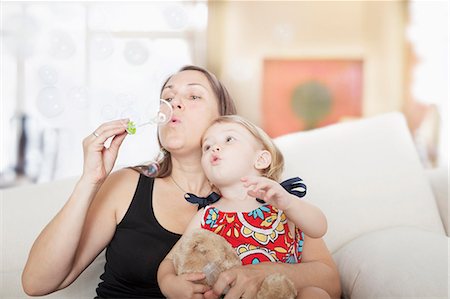 Mother and daughter sitting on the couch and blowing bubbles in the living room Stock Photo - Premium Royalty-Free, Code: 6116-07236198