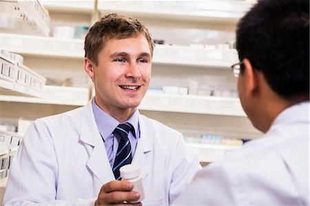 simsearch:6116-07235577,k - Smiling young pharmacist showing prescription medication to a customer Foto de stock - Sin royalties Premium, Código: 6116-07236112