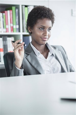 Portrait of young smiling businesswoman sitting at a table and holding a pen Photographie de stock - Premium Libres de Droits, Code: 6116-07236264