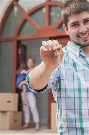 Father smiling and holding the keys to the new house, family in the background Stock Photo - Premium Royalty-Free, Code: 6116-07236224