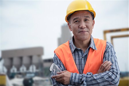 Portrait of proud worker with arms crossed in protective workwear outside of a factory Stock Photo - Premium Royalty-Free, Code: 6116-07236362