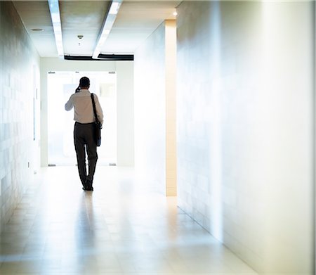 Businessman walking down the corridor on the phone Stock Photo - Premium Royalty-Free, Code: 6116-07236571