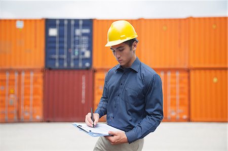 simsearch:630-03482133,k - Smiling young engineer in protective work wear in a shipping yard examining cargo and writing on clipboard Stock Photo - Premium Royalty-Free, Code: 6116-07236595