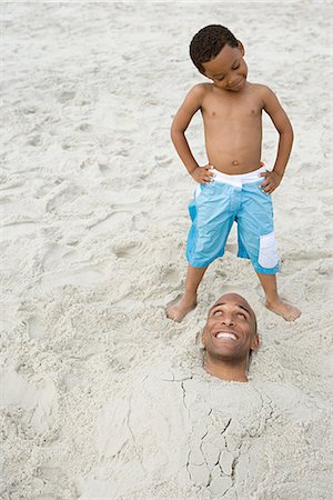 people buried in the sand - Son looking at father buried in sand Stock Photo - Premium Royalty-Free, Code: 6116-08915807