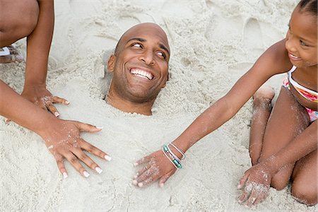 family relaxing with kids in the sun - Family burying father in sand Photographie de stock - Premium Libres de Droits, Code: 6116-08915810