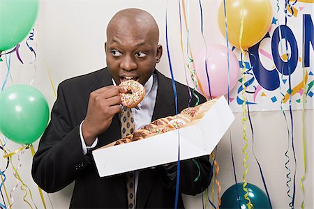 Businessman secretly eating doughnuts Stock Photo - Premium Royalty-Free, Code: 6116-09013669