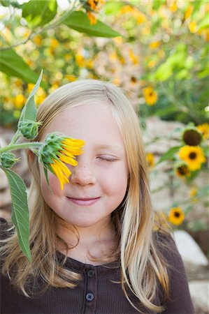A Child Standing In A Flower Garden. A Girl With Her Eyes Closed With Sun Flower In Front Of Her Eye. Stock Photo - Premium Royalty-Free, Code: 6118-07121888