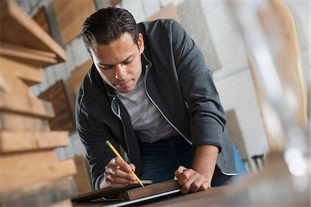 simsearch:6118-07121806,k - A Young Man In A Workshop Which Uses Recycled And Reclaimed Lumber Using Paper And Pen To Keep Records. Stockbilder - Premium RF Lizenzfrei, Bildnummer: 6118-07121801