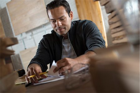 simsearch:6118-09148280,k - A Young Man In A Workshop Using Paper And Pen To Keep Records. Photographie de stock - Premium Libres de Droits, Code: 6118-07121802