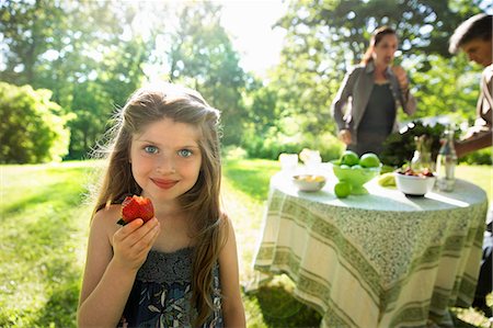 A Young Girl Holding A Large Fresh Organically Produced Strawberry Fruit. Two Adults Beside A Round Table. Foto de stock - Sin royalties Premium, Código: 6118-07121830